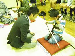 日本の擦弦楽器・胡弓を体験する少年と指導する若手奏者・木場大輔さん